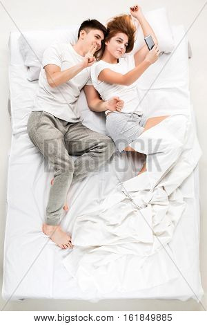 The young lovely couple lying in a bed with phone, love lconcept, top view