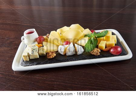 Cheese love. Cheese plate with Dorblu Brie Gouda and Camembert on a plate served with walnuts and grapes on a restaurant table