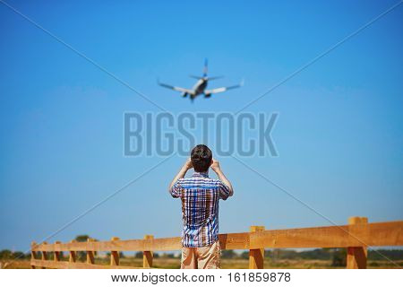 Man is looking at the glide path and landing plane or taking a photo of it. Aircraft spotting concept