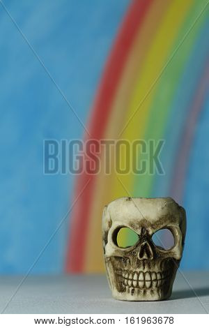 Human skull with a blue sky and rainbow background, a symbol of death, vanitas and horror; portrait format.