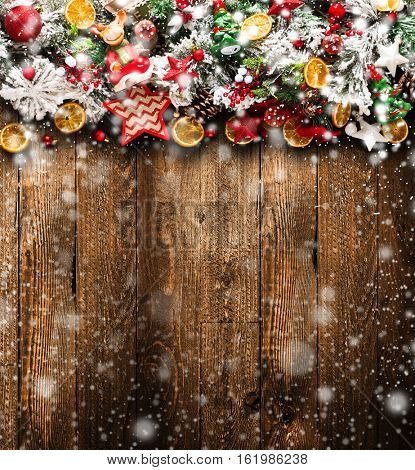 Merry Christmas Frame with Snow and wood green pine, colorful baubles, knots with berries,stars, orangesand other seasonal stuff over an old wooden aged background