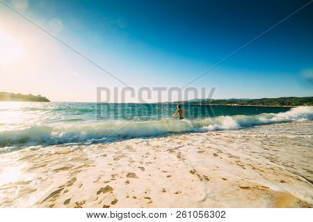 Beach On The Mediterranean In A Clear Sunny Day, Greece, Halkidiki. Young Tourist Swims In Big Waves