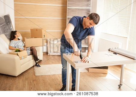 Smiling Man Putting Together Self Assembly Furniture In New Home.