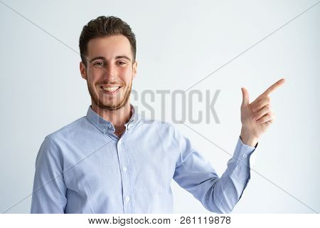 Cheerful Manager Presenting Product. Young Man In Office Shirt Pointing Finger At Copy Space Away An