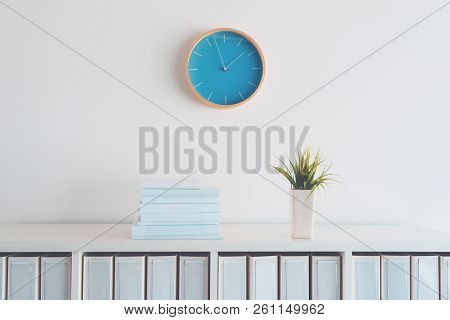 Modern Bright Business Office Interior Detail Depicting Wall Clock And Shelf With Books, Plant And F