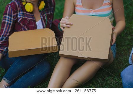 Two Gril Have The Boxes With Pizza On Their Legs. Two Tudents Open The Ordered Food Sitting In The P