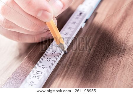 Male Hand Making A Mark At The Measuring Point Of A Folding Yardstick On A Wooden Board