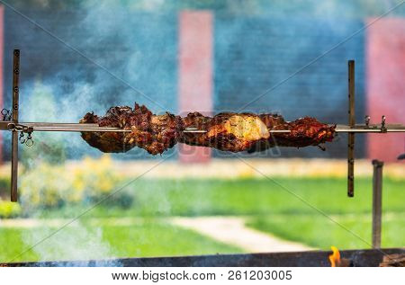 Meat From Pork Prepares On A Skewer On The Fire In The Yard In The Summer. Smoke Gives Piquancy To M
