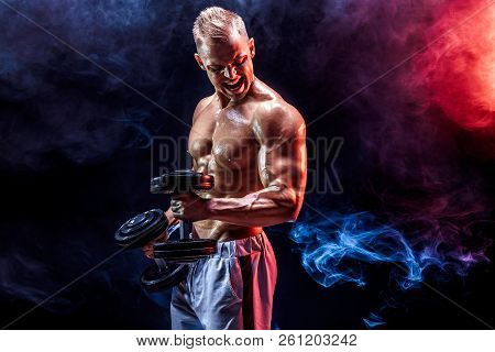 Topless Man Exercising Biceps With Dumbbells Posing In Studio Fuul Of Colored Smoke