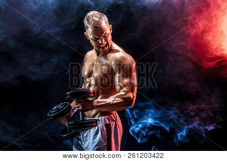 Topless Man Exercising Biceps With Dumbbells Posing In Studio Fuul Of Colored Smoke