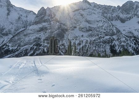 Sunny Winter Day With The Snowy Peaks Of The Alps Mountains, Fir Trees, And A Thick Layer Of Ice And