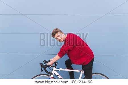 Smiling Young Student Sitting On A White Sixth Bike On A Background Of A Blue Wall And Looking At Th