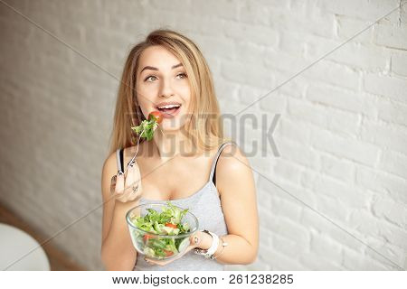 Attractive Happy Woman Holding Bowl Of Fresh Vegetable Salad In Hands Eating With The Fork, Enjoing 
