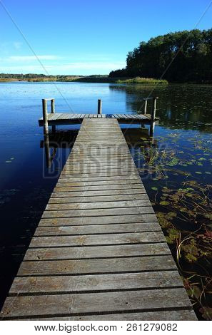 Long wooden bridge in lake with calm water and blue sky in Sweden, Scandinavia, Europe. Peaceful outdoor image on Malaren lake in Vastmanland