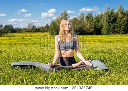 Young Female With Open Arms And Long Blond Hair Relaxes In Yoga Pose In Green Nature