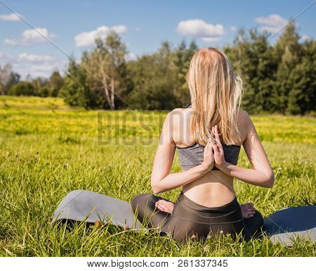 Young Female With Open Arms And Long Blond Hair Sitting Back And Relaxes In Yoga Pose In Green Natur