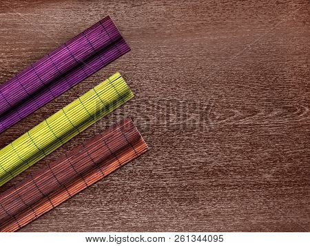 Bamboo Mats Of Violet, Green, Brown Color Rolled Into Rolls Lie On A Wooden Background Horizontally 