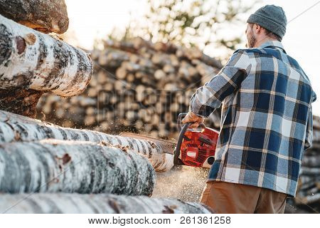 Professional Strong Lumberman Wearing Plaid Shirt Sawing Tree With Chainsaw For Work On Sawmill. Saw