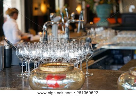 Bar Rack With Wine Glasses. The Barmaid Serves Wine Glasses For A Party In A Bar, A Hotel Restaurant
