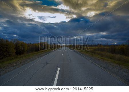Deciduous Autumn Forest Grows Along An Asphalt Road With A Discontinuous Divided Strip Against The S