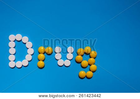 Word Drugs From Color Capsules On The Blue Background. Top View Copy Space Pattern