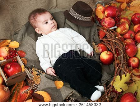 autumn concept - child boy lie on yellow leaves with fruits and vegatbles, red apples and pumpkins