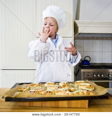 Un piccolo ragazzo, vestito come uno chef, leccare le dita, che illustra quanto è buono il pane è cotto sarà t