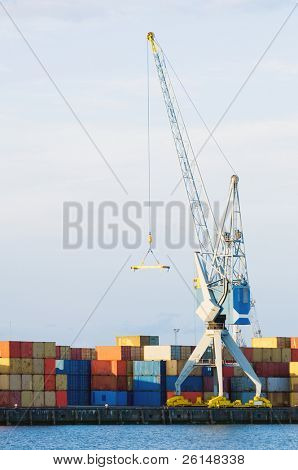 En stor last kran står vid porten framför buntar med behållare. Det finns ingen synlig i den
