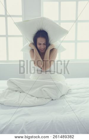Young caucasian woman covering her head and ears with pillows.