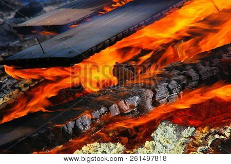 Closeup Photo Of Wood Burning In Fire. One Rusty Nail Still Standing In One Piece Of Wood.
