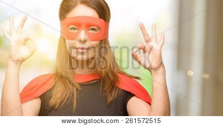 Middle age super hero woman wearing red mask and cape doing ok sign gesture with both hands expressing meditation and relaxation