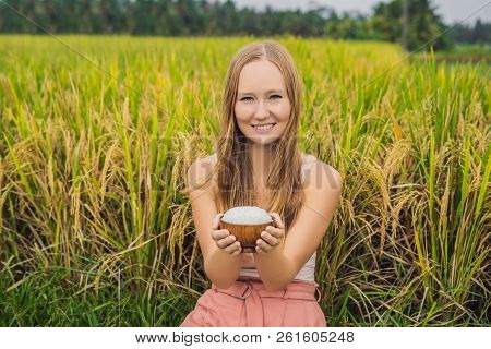 A Woman Is Holding A Cup Of Boiled Rice In A Wooden Cup On The Background Of A Ripe Rice Field
