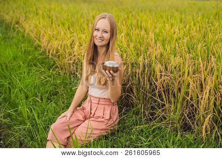 A Woman Is Holding A Cup Of Boiled Rice In A Wooden Cup On The Background Of A Ripe Rice Field