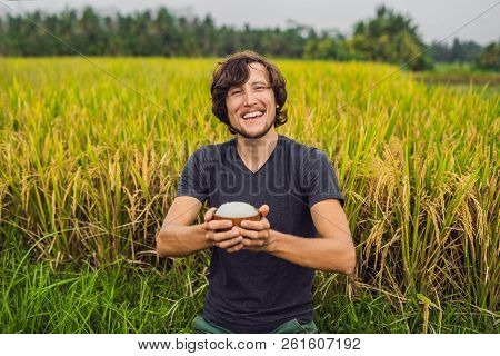 Man Is Holding A Cup Of Boiled Rice In A Wooden Cup On The Background Of A Ripe Rice Field