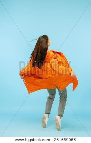 The Back View Of Young Girl Posing At Studio In Autumn Jacket Isolated On Blue. Human Emotions. Conc