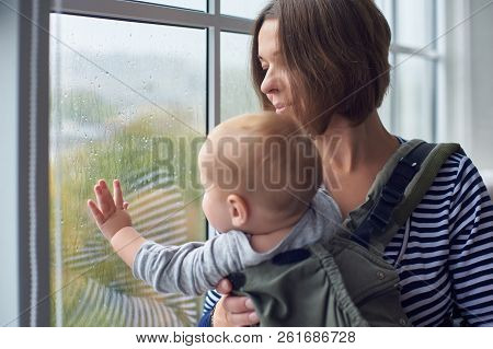 Mother With Ergobaby Carrying Toddler At Home.