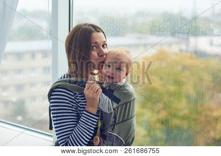 Mother With Ergobaby Carrying Toddler At Home.