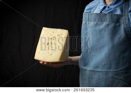 Woman Holding Slice Of Cheese Wearing Blue Apron On Dark Background