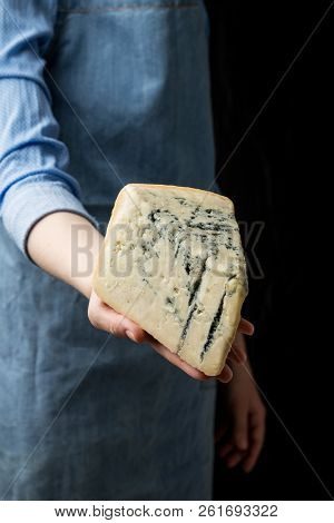 Woman In Apron Holding Piece Of Blue Cheese Gorgonzola On Dark Background
