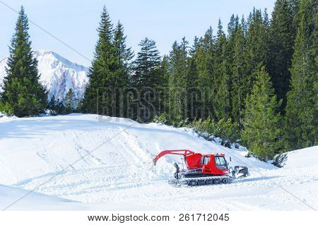 Winter Activity In The Mountains With A Red Snow Groomer Surrounded By Snow And Green Fir Forest In 