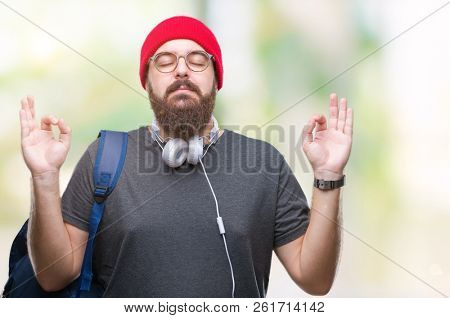 Young hipster man wearing red wool cap and backpack over isolated background relax and smiling with eyes closed doing meditation gesture with fingers. Yoga concept.