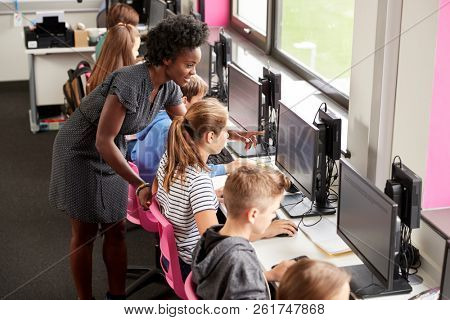 Teacher Helping Female Pupil Line Of High School Students Working at Screens In Computer Class