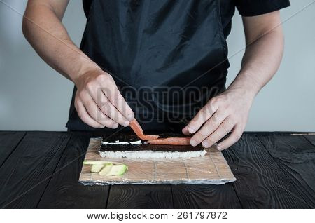 Process of making maki sushi. Cook chef hands preparing rolls with cheese, avocado and sesame seeds
