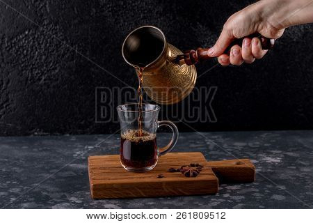 Cup And Pot Of Coffee And Coffee Beans On A Wooden Board. Female Hand Pouring Traditional Turkish Co