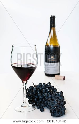 Glass Of Red Wine With A Bottle And A Cluster Of Black Grapes On White Table. Selecive Focus.