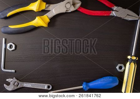 A Black Wooden Background With Various Hardware Tools: Wrench, Hexa Key, Nut, Cutting Pliers, Pliers