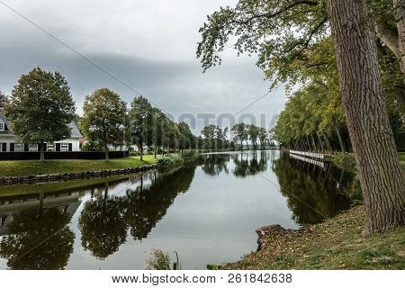 Sluis, Zeeland, Netherlands - September 22, 2018: Gray Sky And Green Bordering Trees Reflected In Qu