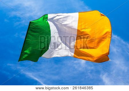 Irish Flag Fluttering In A Brisk Breeze Against A Bright Blue Sky.