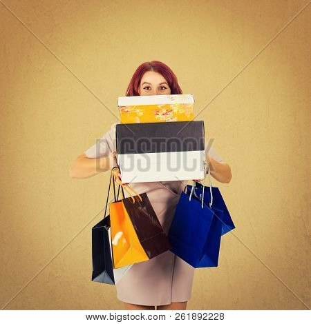 Cheerful Woman Shopaholic Hiding Behind A Pile Of Boxes, Carrying Shopping Bags Isolated Over Bown B