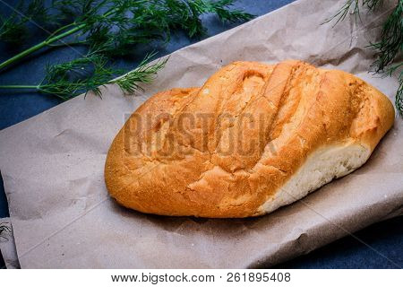 A Loaf Of White Bread On Brown Kraft Paper, Surrounded By Dill On A Dark Background.